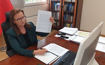 podpisanie umowy z Uniwersytetem Ekonomicznym w Katowicach - foma zdalna. Prezez ZUS siedzi za biurkie, w ręku trzyma kartkę z umową, przed nia monitor.